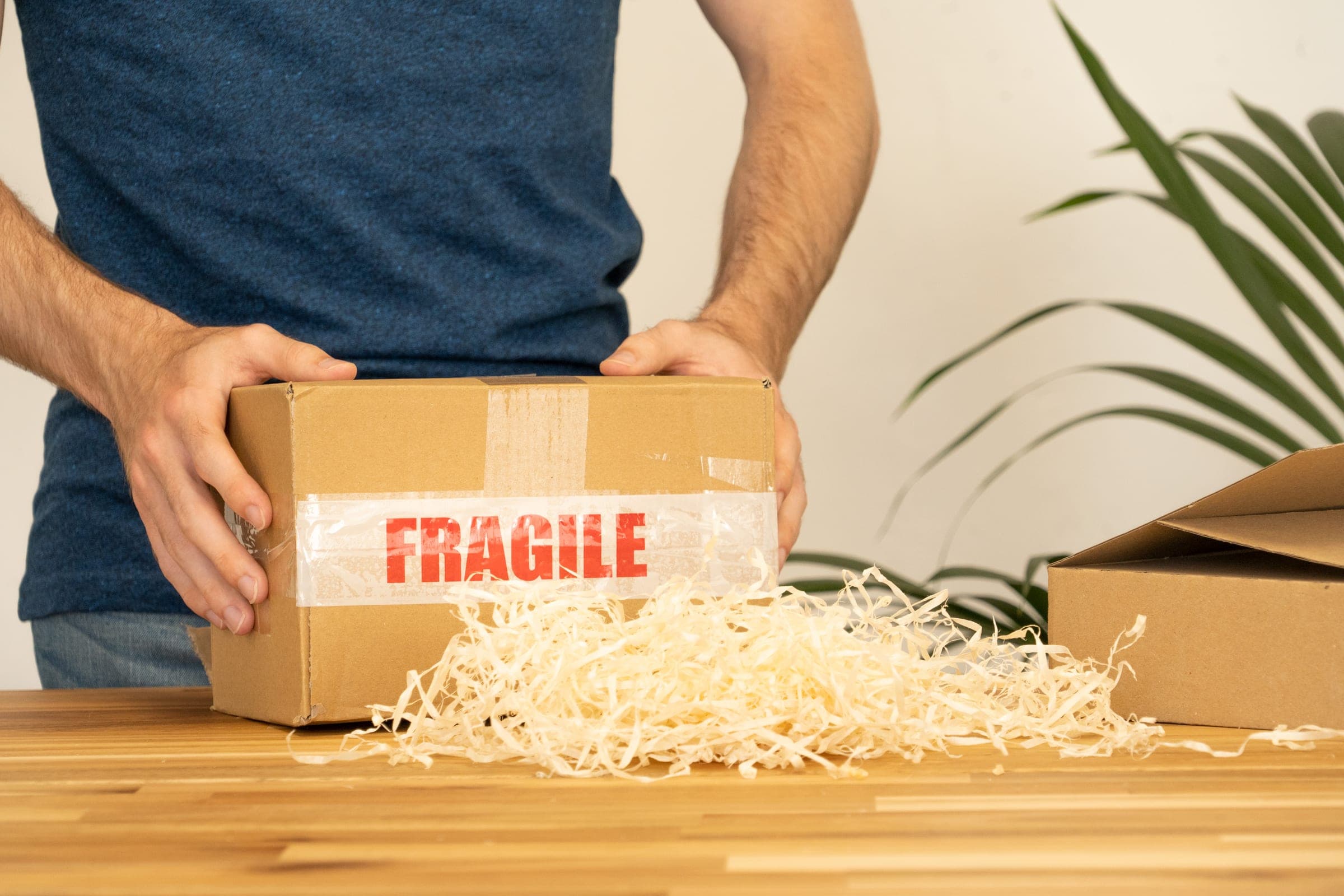 Un colis marqué fragile, rempli de frisure de bois, sur un plan de travail