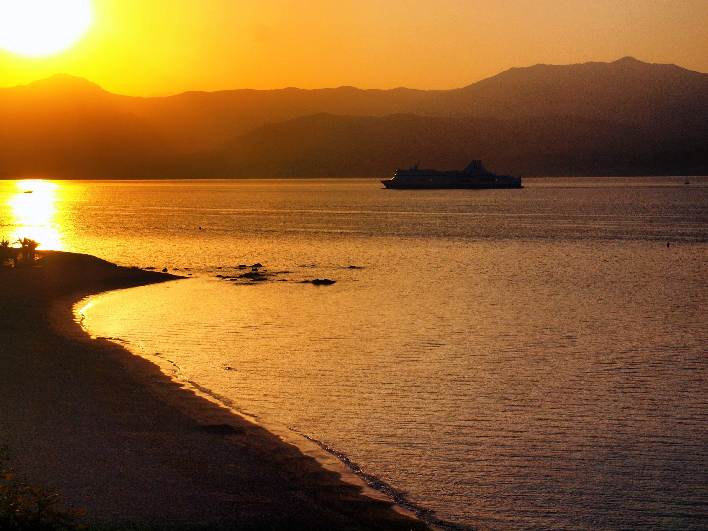 Un navire entre dans le golfe d'Ajaccio au lever du soleil, la mer dorée et les montagnes en contre-jour